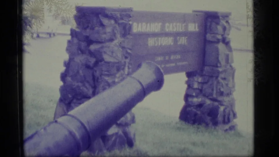 1977 Alaska 8mm frame showing a foreground cannon aimed toward the Baranof Castle Hill Historic Site sign.