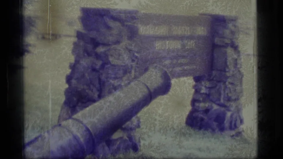 1977 Alaska 8mm frame of the Baranof Castle Hill Historic Site sign and cannon with heavy film wear and color shift.