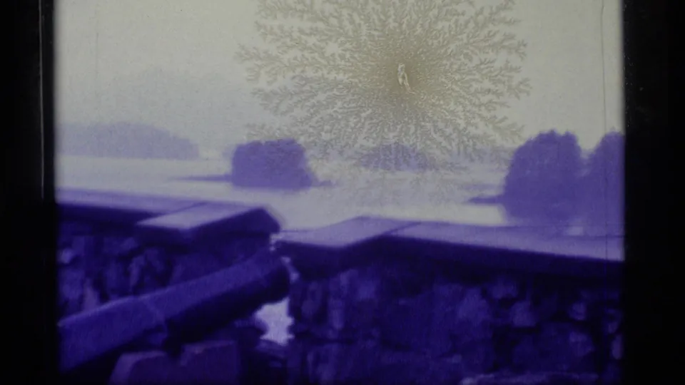 1977 Alaska 8mm still showing a visitor viewpoint over water, with stonework, cannon, islands, and blue-purple film cast.