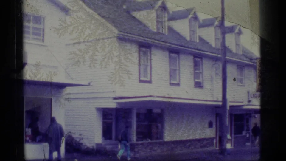 1977 Alaska Super 8 frame showing a wooden multi-story building, sidewalk pedestrians, and partial storefront signage.