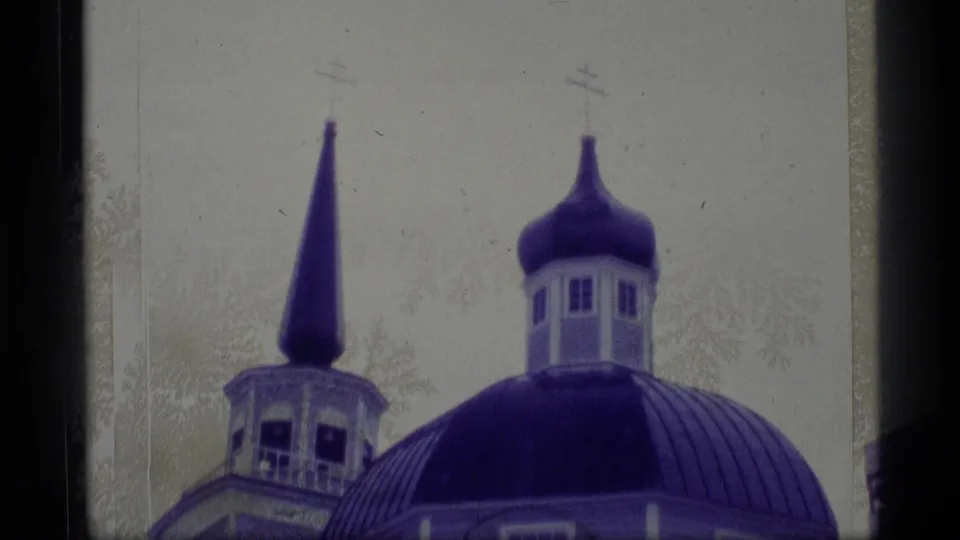 1977 Alaska 8mm frame showing a domed church roof, onion-shaped cupola, adjacent steeple, and pale overcast sky in purple-tinted film color.