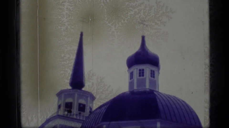 1977 Alaska 8mm frame showing a blue domed church roof, cupola, and pointed spire against a pale snowy background.