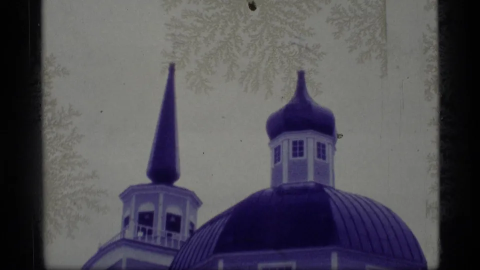 1977 Alaska 8mm frame with a blue church dome, rounded cupola, and narrow spire framed by film borders.