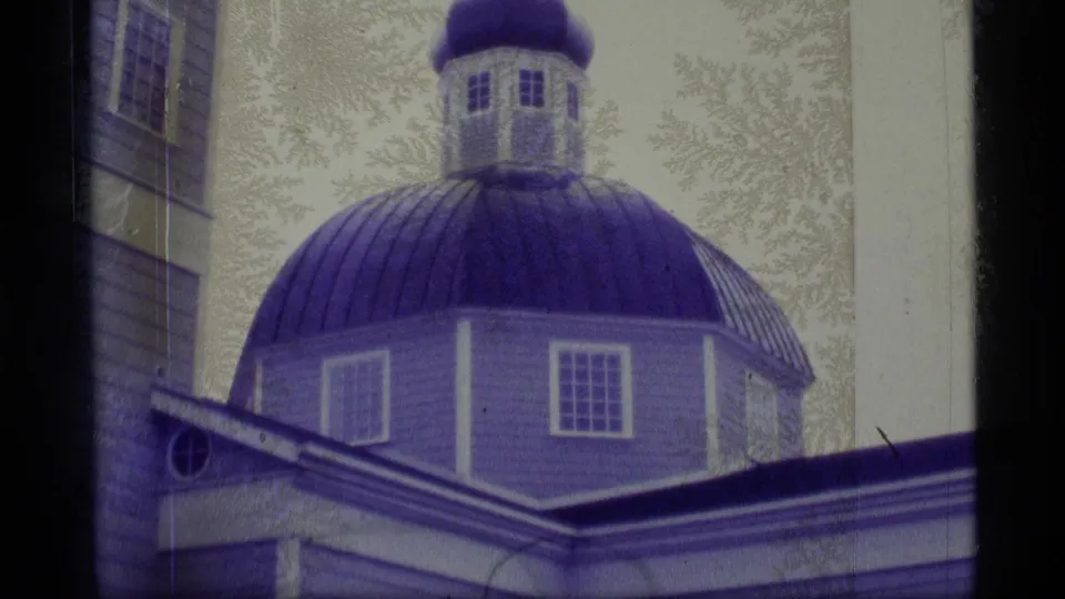1977 Alaska 8mm frame showing the church's blue dome, cupola, windows, adjacent wall, and dark roofline.