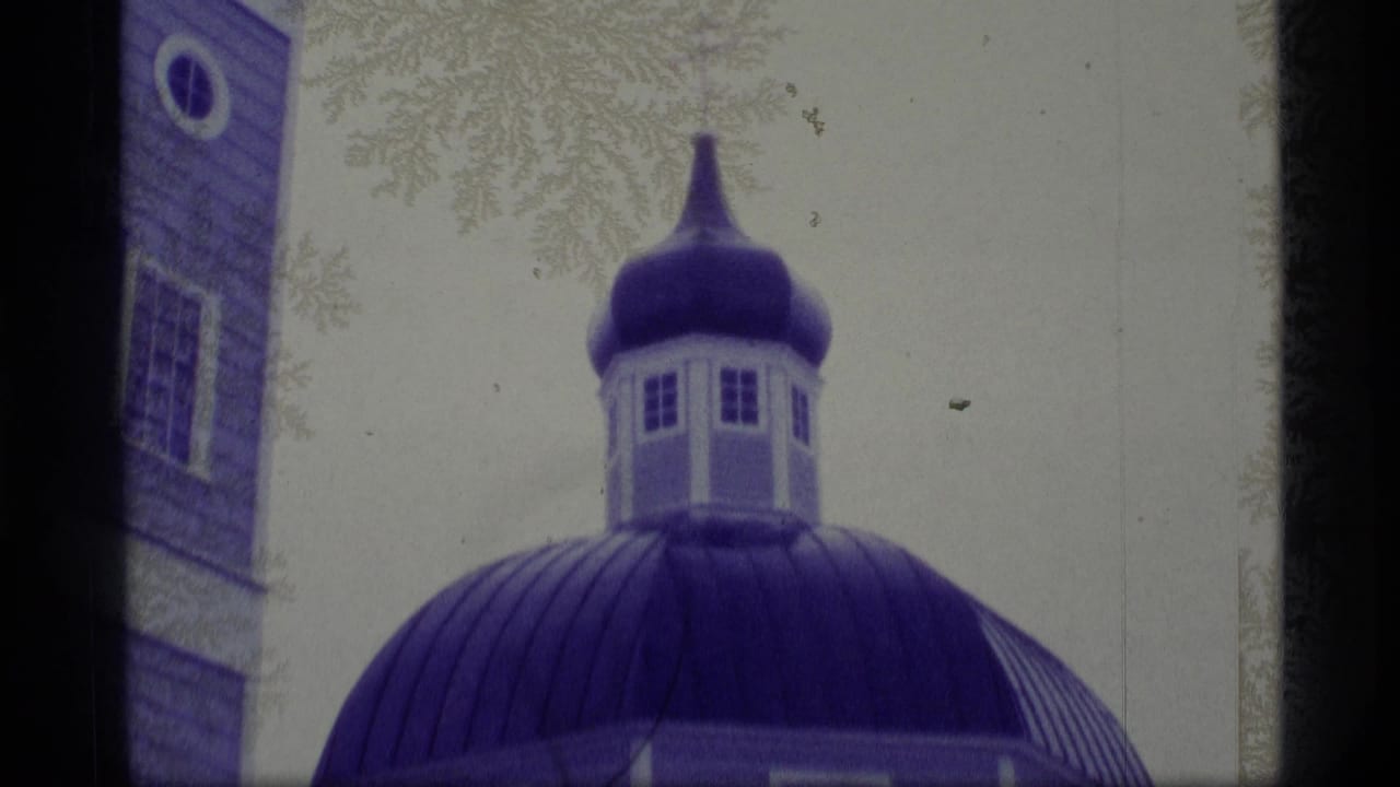 Blue onion church dome and partial wall seen through frosty branches.