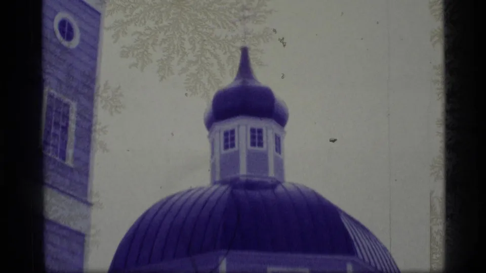 1977 Alaska 8mm frame showing a blue onion dome with a cross area partly out of view, beside a church wall and frosty branches.