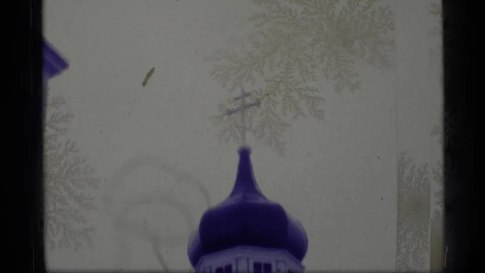 1977 Alaska home-movie frame with the upper portion of a blue onion dome and cross visible against pale sky and frosty branches.