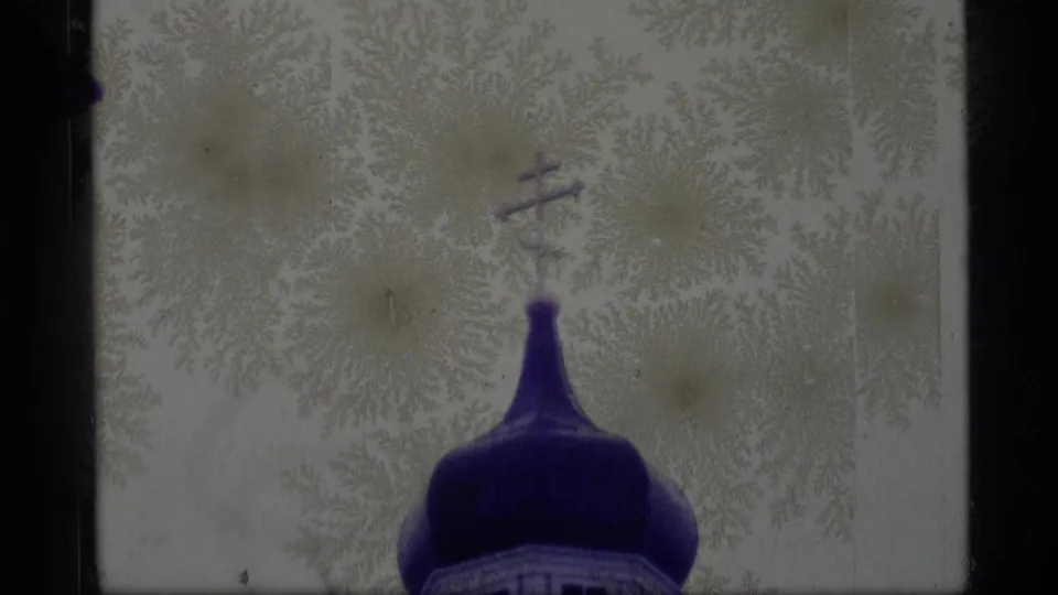 1977 Alaska 8mm frame showing a blue onion church dome topped by a cross, with pale frosty branches filling the background.