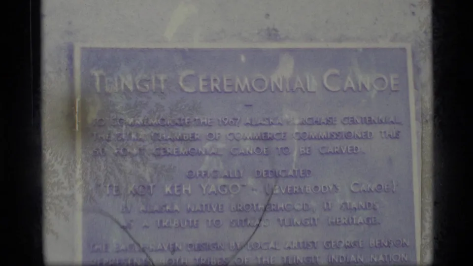 Close 1977 Alaska 8mm view of a commemorative plaque headed Tlingit Ceremonial Canoe, with faded small text below.