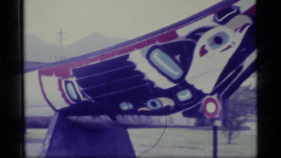 1977 Alaska 8mm frame showing the carved and painted end of a ceremonial canoe, with mountains faintly visible behind it.
