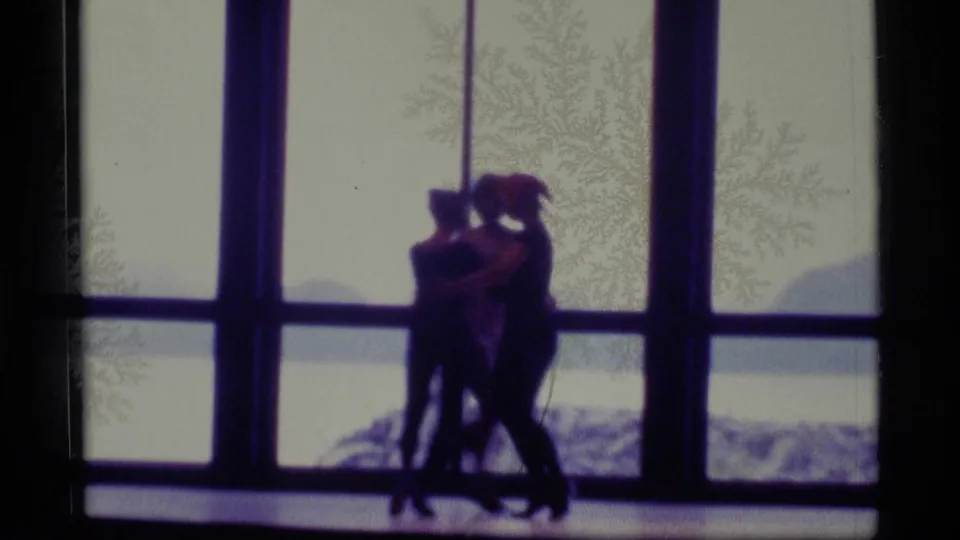 Silhouetted dancers in the Alaska 1977 clip stand close together near tall windows, with water or land faintly visible outside.