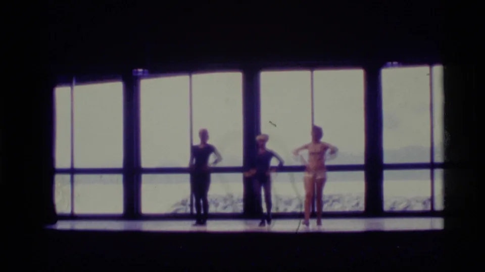 Three dancers in leotards are silhouetted against bright Alaska window light, with snowy scenery visible behind the stage.