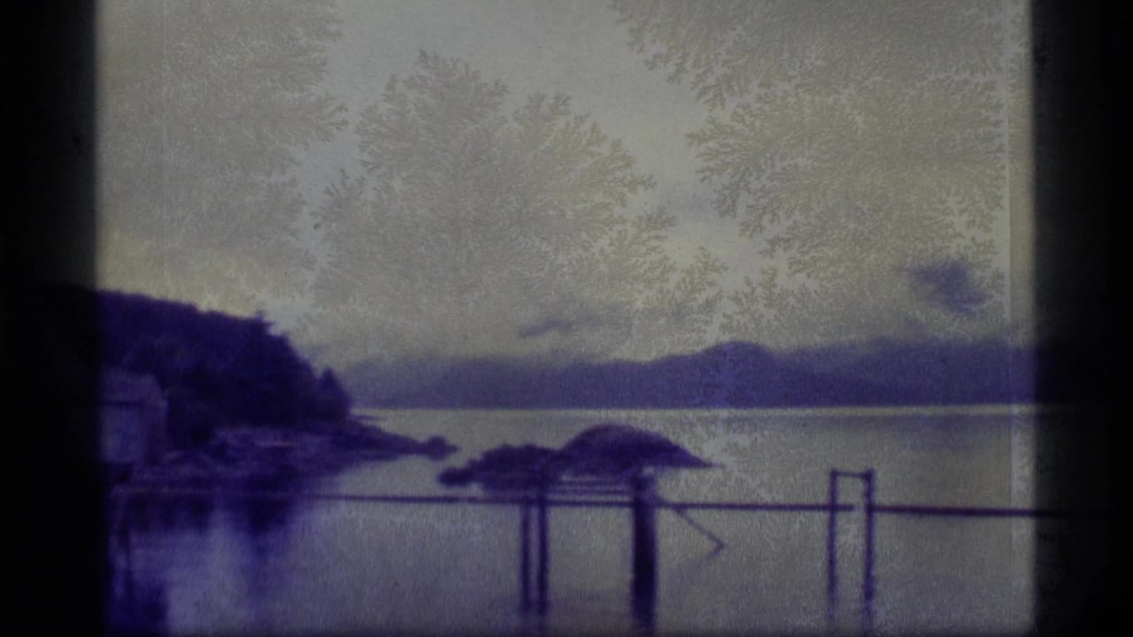 Calm waterway with low islands, distant hills, and dock railings in front.