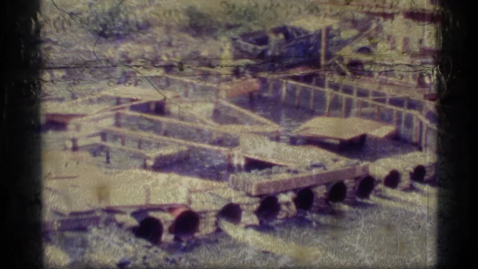 Faded 1977 8mm frame from the Alaska-labeled footage showing a wider waterlogged area with wooden platforms, railings, and equipment-like structures.