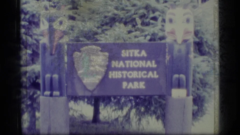 1977 8mm frame showing the Sitka National Historical Park sign between carved totem forms and trees.