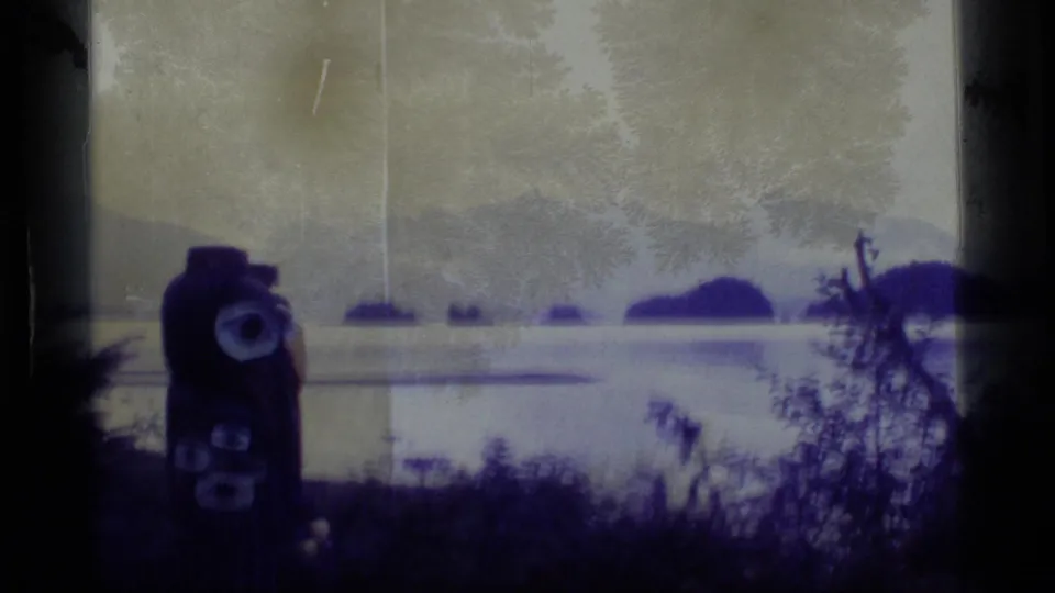 Soft 8mm frame from Alaska in 1977, with the totem pole at left and a pale bay stretching toward wooded islands.