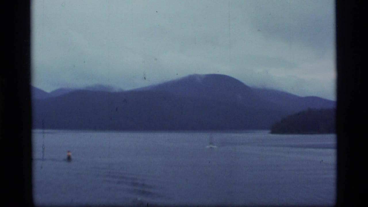 Misty lake with distant mountains, a buoy, and a small boat far across the water.