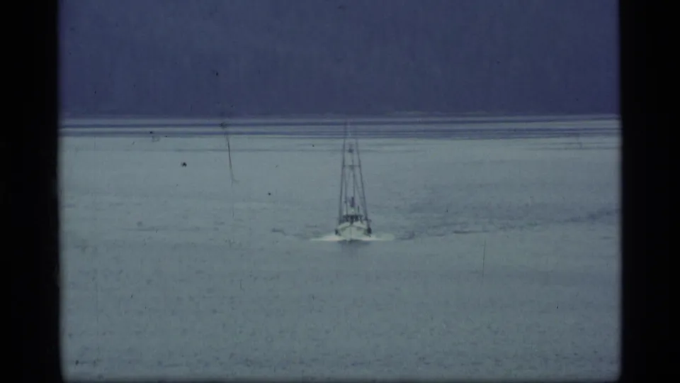 1977 Alaska 8mm frame showing a sailboat centered on gray lake water against soft, misty mountain forms.