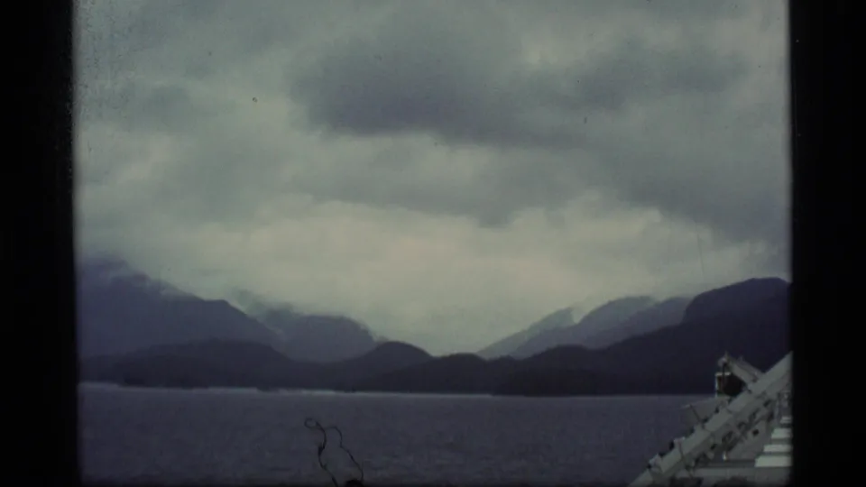 1977 Alaska 8mm frame showing layered dark ridges across water, with a small vessel or railing detail visible at the lower right.
