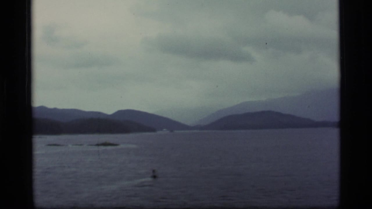 Misty lake with forested islands and distant mountains seen past dark frame edges.