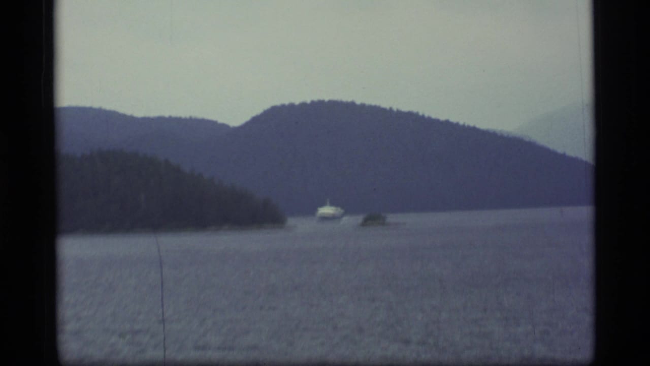 Distant boat on a calm lake between forested shores and low mountains.