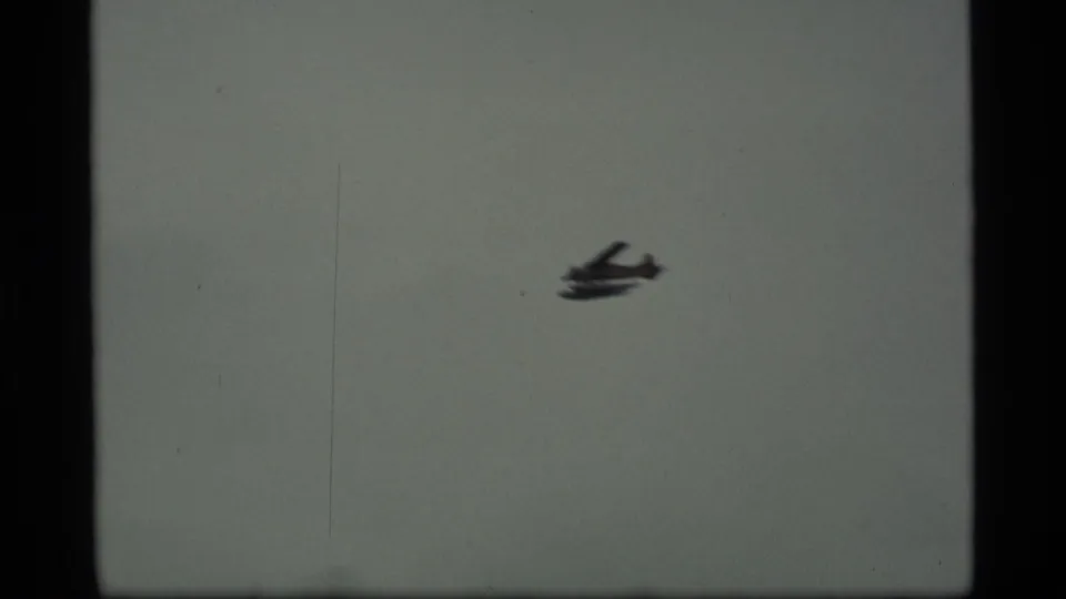 Small propeller plane appears against a gray sky in 1977 Alaska home-movie footage, with visible film borders and scratches.