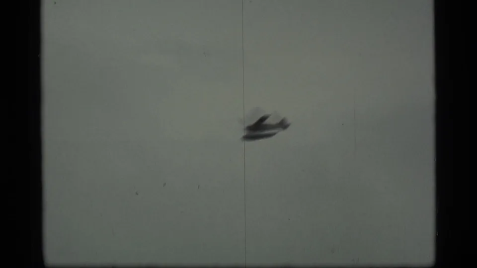 A small aircraft flies across a muted gray sky in the Alaska travel clip, seen through soft 8mm film texture.