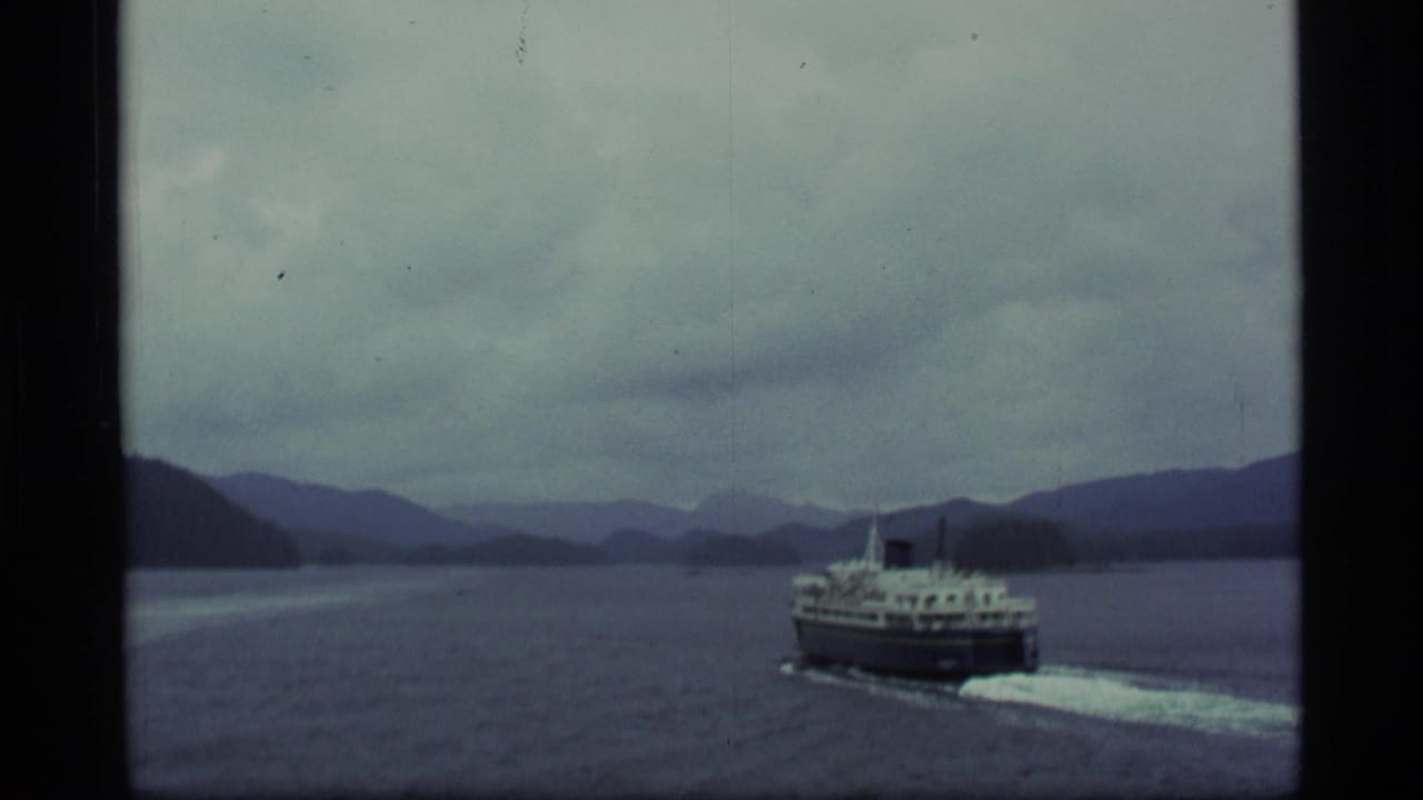 Passenger ferry moving across calm water with mountains in the distance.