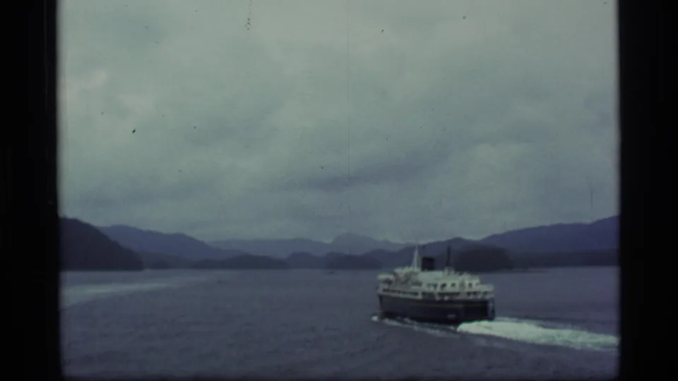 1977 Alaska 8mm frame showing a passenger ferry crossing blue-gray water before misty mountains.