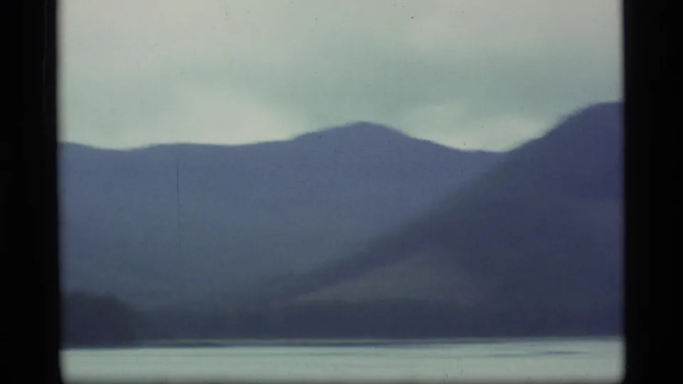 Vintage Alaska 8mm landscape frame showing layered mountain ridges, mist, and a quiet waterway.