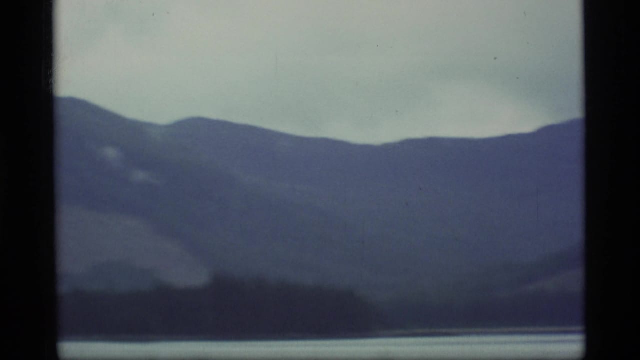 Misty mountain ridge and dark shoreline across calm water, framed by film borders.