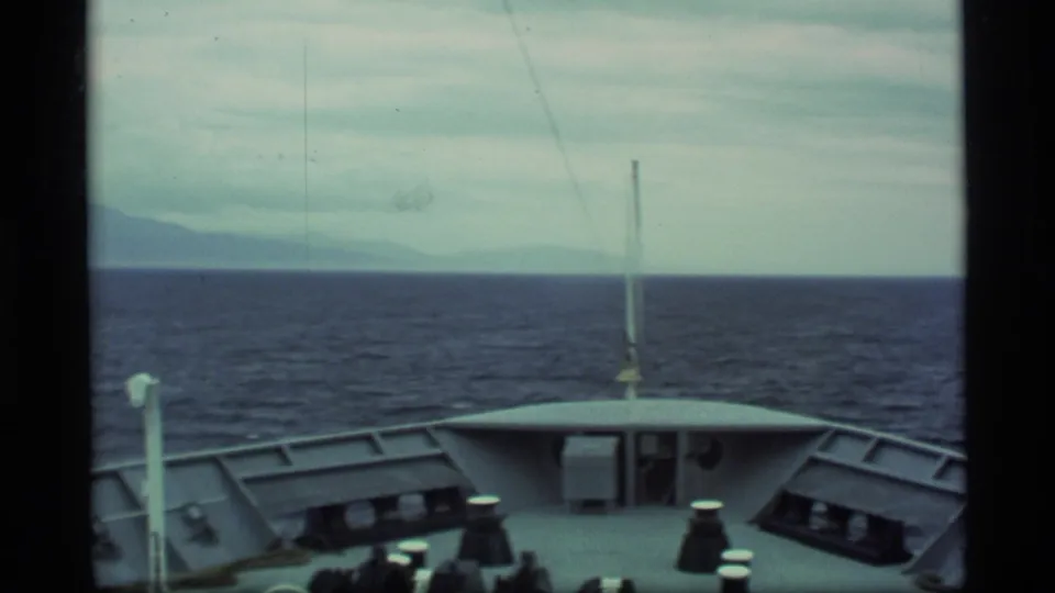 1977 Alaska home-movie view from the cruise ship bow across dark water toward a muted mountain horizon.