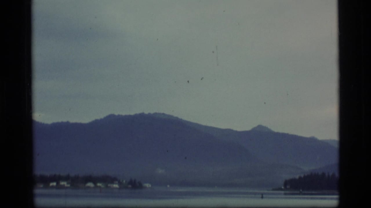 Mountain range and shoreline seen across water, with dark film borders visible.