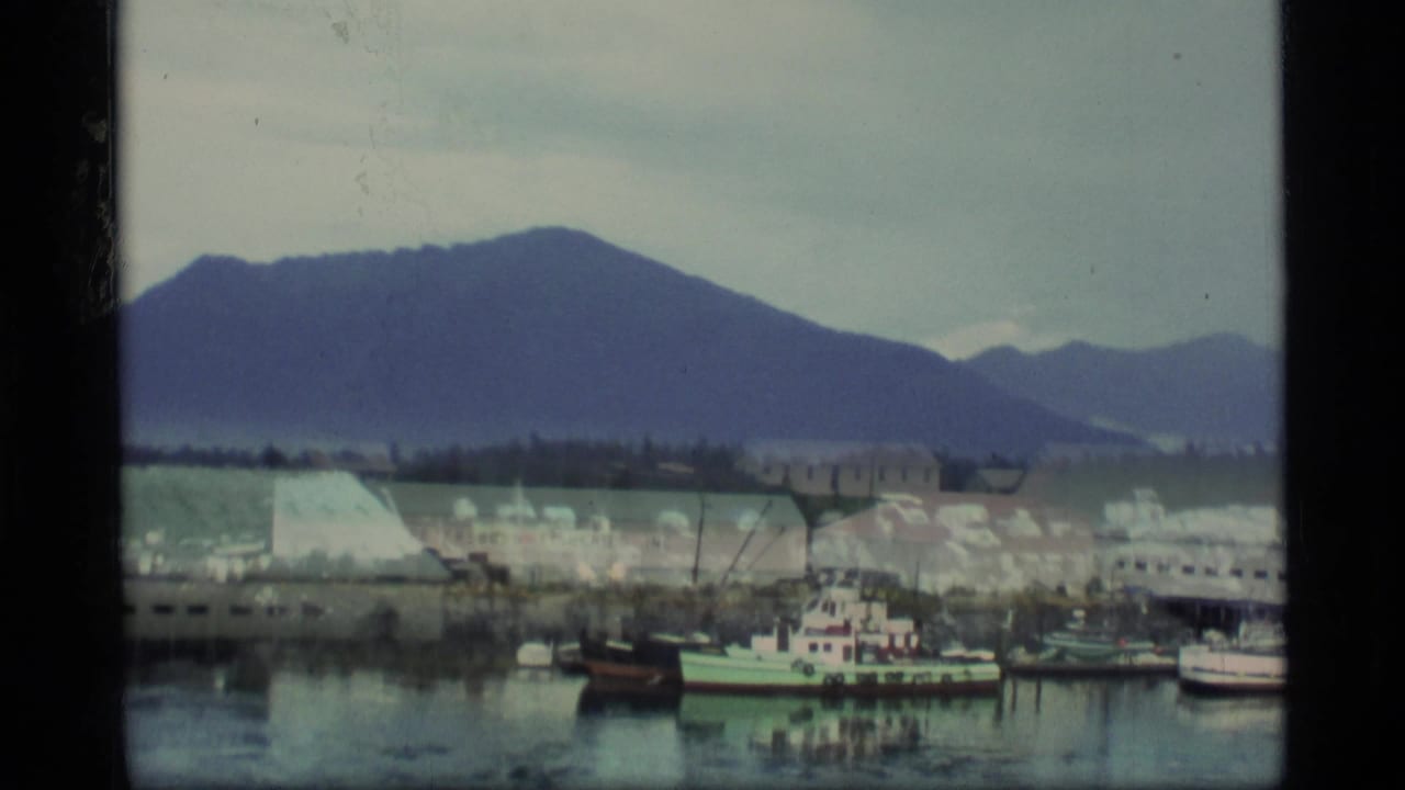 Harbor buildings and small boats beneath dark mountains in an overcast coastal town.