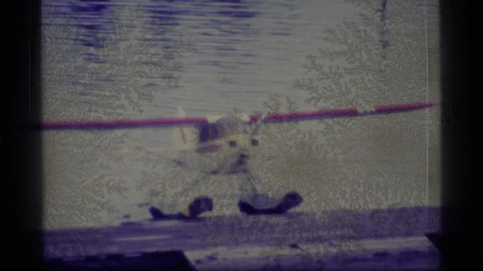1977 Alaska 8mm frame showing a floatplane at the water’s edge, with soft focus, heavy grain, and dark gate borders.