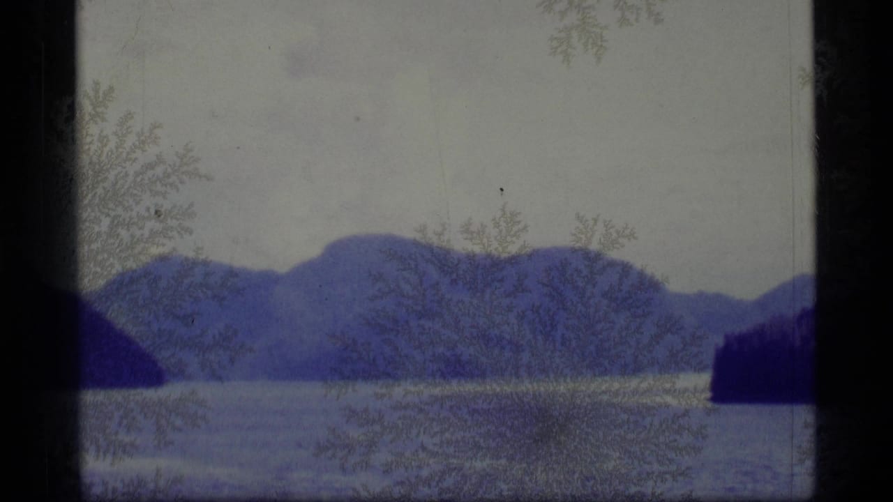 Distant mountains across a calm body of water with frost-like marks over the film frame.