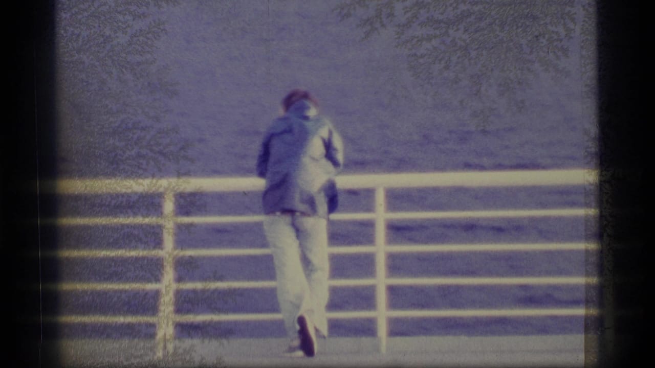 1977 Alaska 8mm frame showing a man in a jacket and light pants at a ship railing, looking over open water.