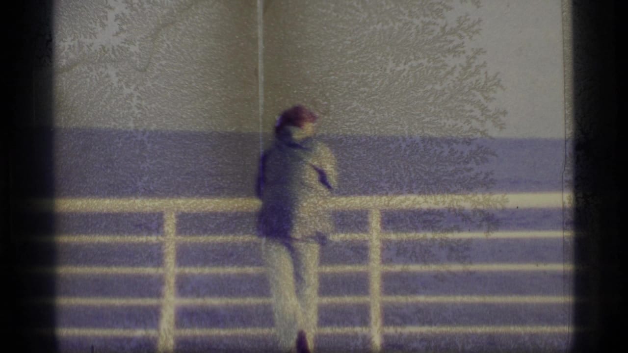 Man near a white railing on a ship deck with water in the background.