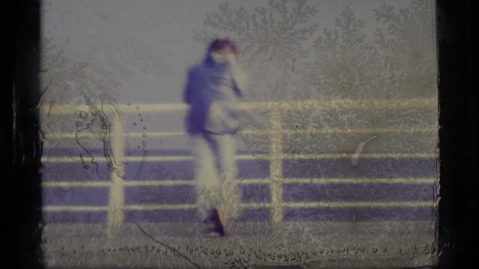 1977 Alaska 8mm frame with a blurred man at a ship railing, surrounded by cool-toned grain and visible film surface marks.