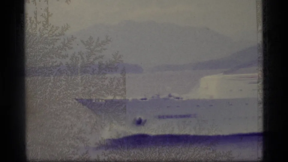 1977 Alaska 8mm frame showing open water, a distant mountainous shoreline, and heavy film texture from a shipboard viewpoint.