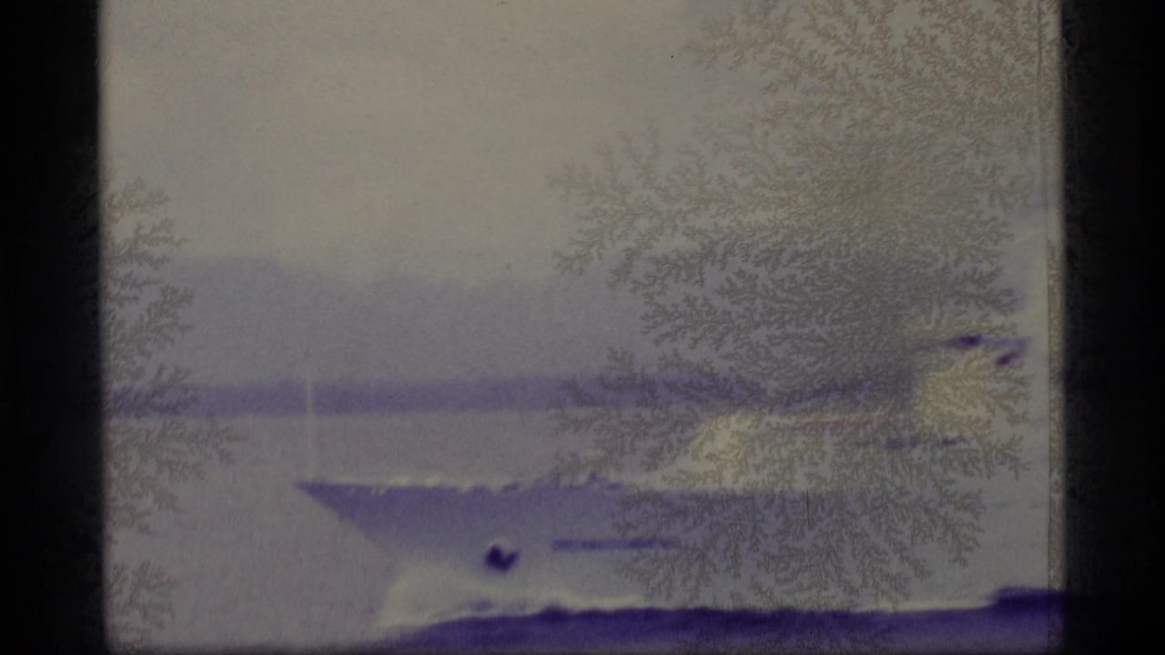 1977 Alaska home-movie frame showing a white passenger ship on calm coastal water under heavy purple staining and emulsion damage.