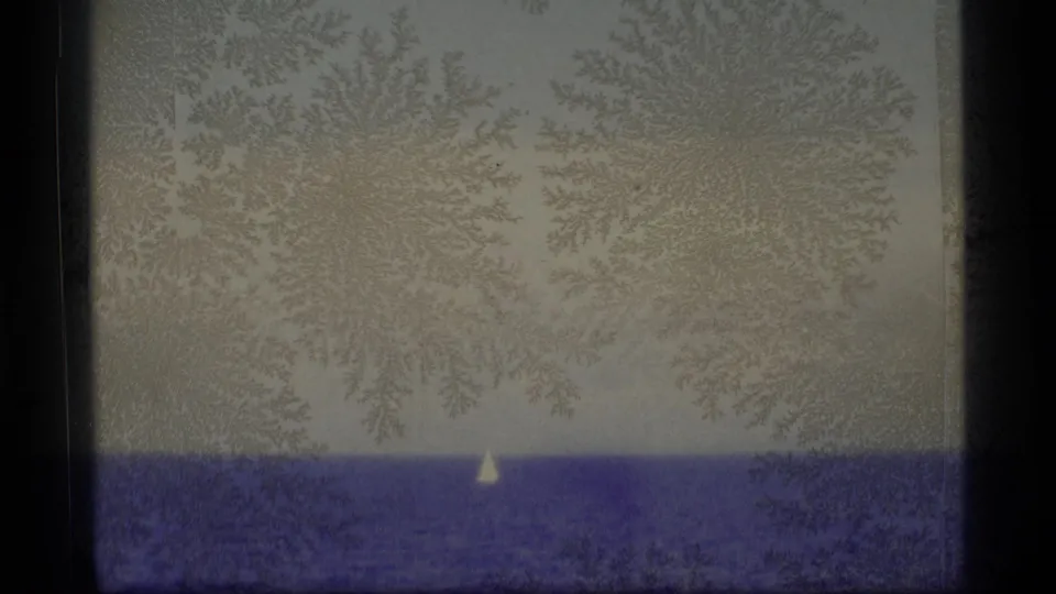 Distant white sailboat on Alaskan water in a soft 1977 8mm home-movie frame with heavy grain and emulsion patterning.