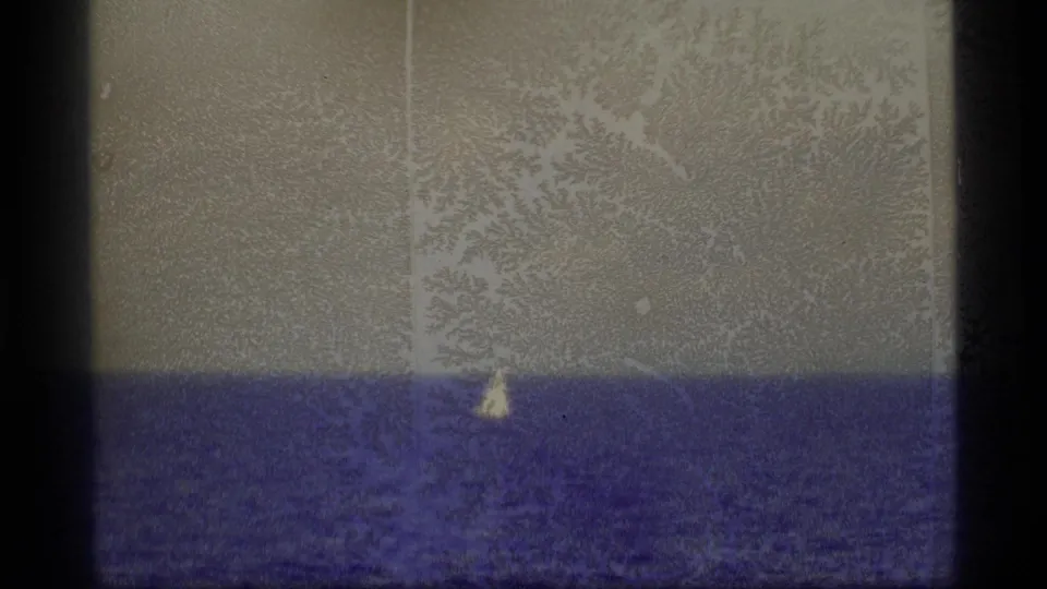 1977 Alaska 8mm view of a tiny sailboat on open water, partly obscured by grain, scratches, and aged-film mottling.