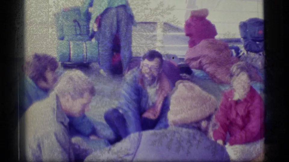 Adults in cold-weather clothing gather on an Alaska boat deck with sleeping bags and backpacks around them.