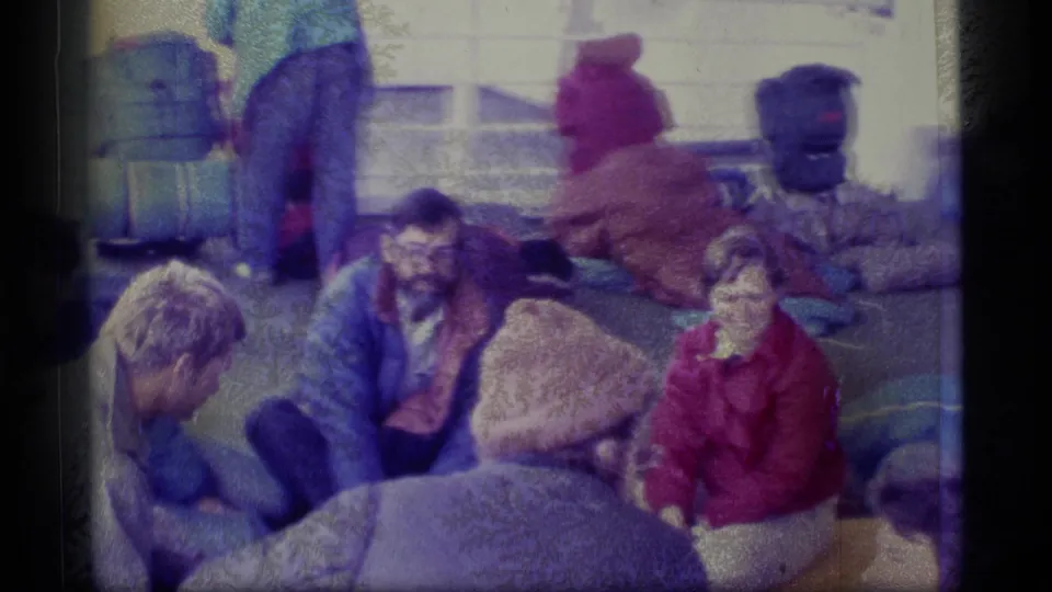 Candid 1977 Alaska deck scene with bundled travelers seated among blankets and travel gear.