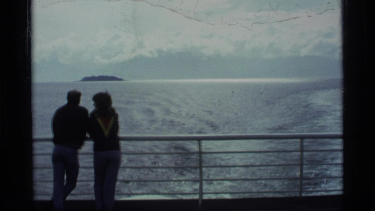 Two silhouetted adults lean near a ship railing with ocean and distant land behind them.