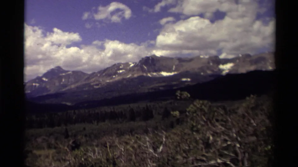 8mm Canada travel frame from 1979 showing a broad mountain panorama with forest, brush, blue sky, and cloud cover.