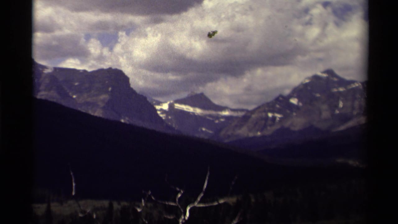 Snow-streaked mountains under heavy clouds, seen through 8mm film gate borders.