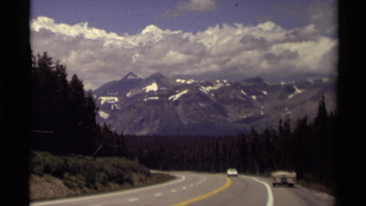 1979 Canadian home-movie view from a moving vehicle on a curving highway toward forested mountains and cloud cover.
