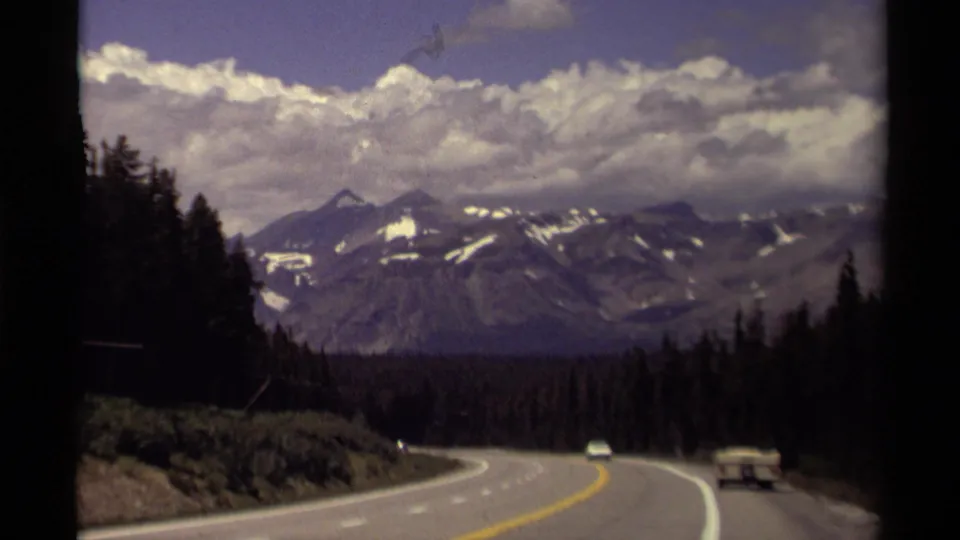 A 1979 Canada travel shot follows a mountain highway with sparse traffic, forest edges, and distant snowy ridges.